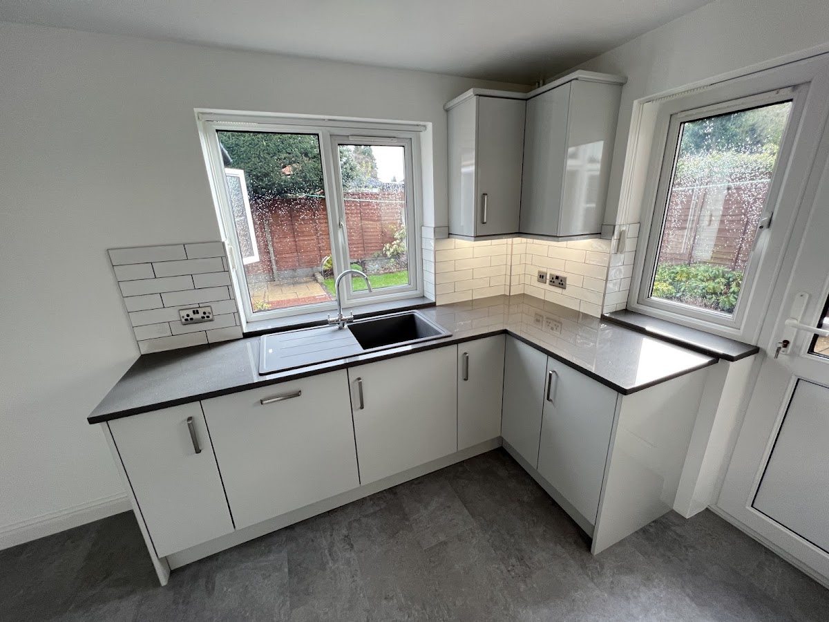 A light grey gloss kitchen with a metro-tiled splashback, dark worktops and corner glazing that floods the room with natural light.